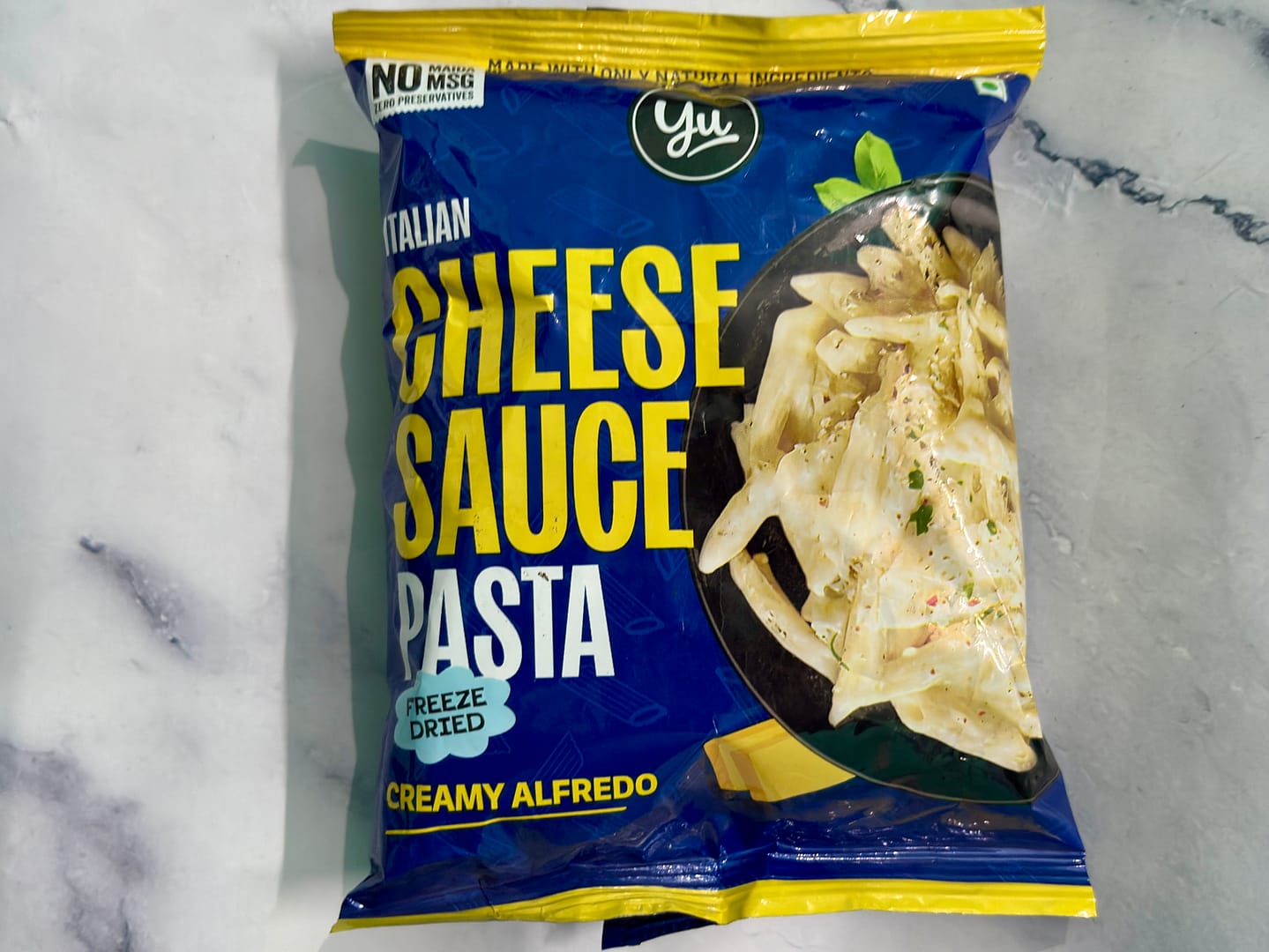 Yu Italian Cheese Sauce sachet and Yu Topping seasoning sachet opened and placed on white marble surface for instant pasta review