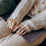 a person wearing knitted sweater holding gray laptop