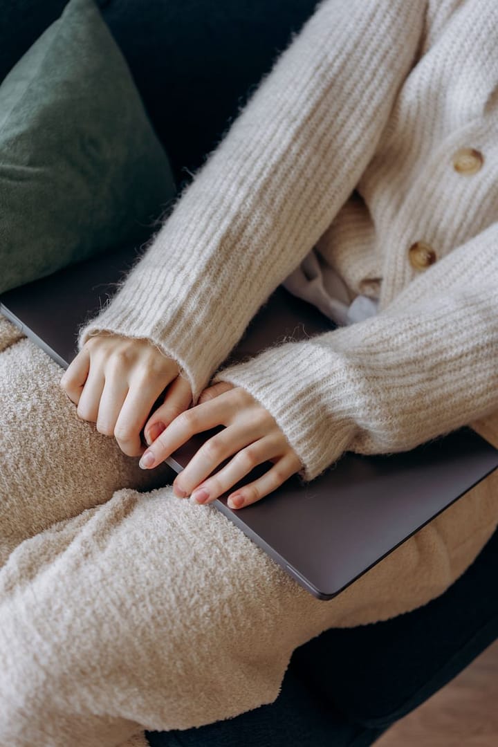 a person wearing knitted sweater holding gray laptop